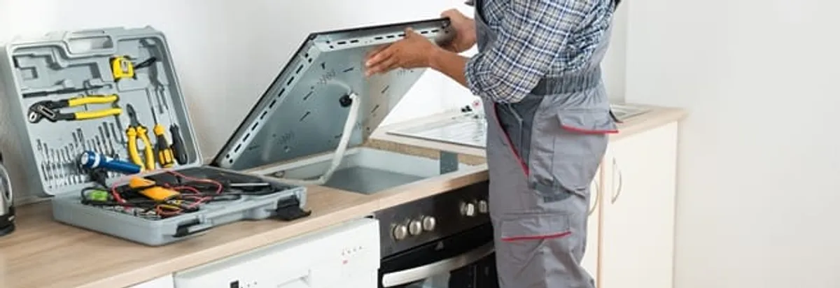 Cooktop repair technician lifting a built-in stovetop for service in Bloomington, IN