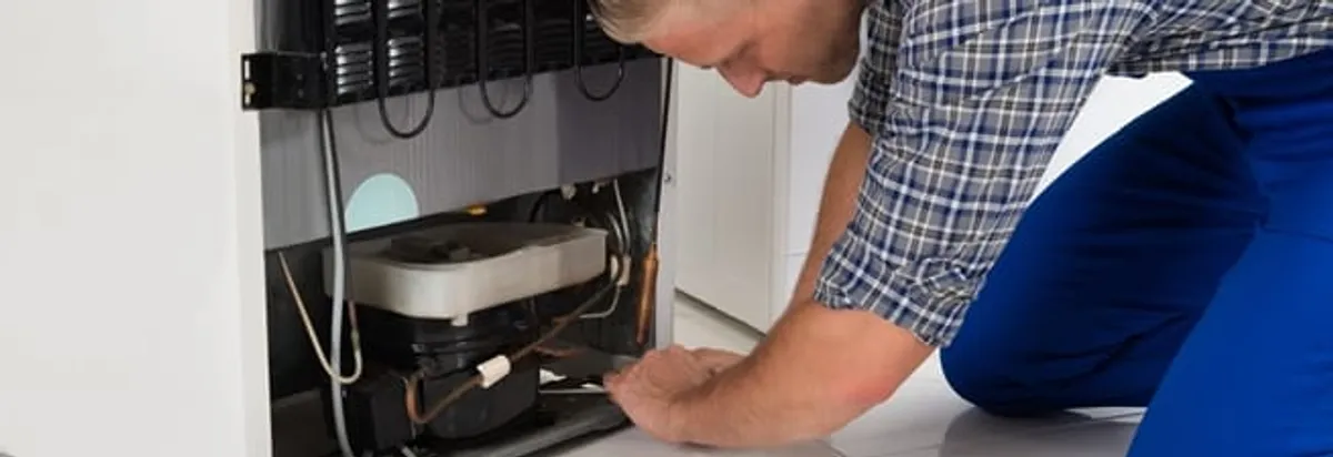 Refrigerator repair technician servicing the compressor and condenser area in Bloomington, IN