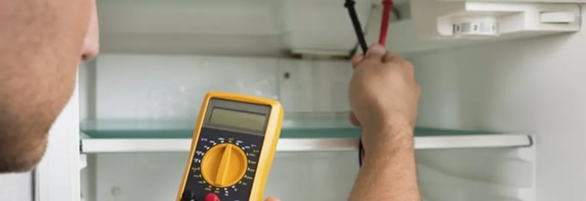 Refrigerator repair technician testing electrical components with a multimeter in Bloomington, IN
